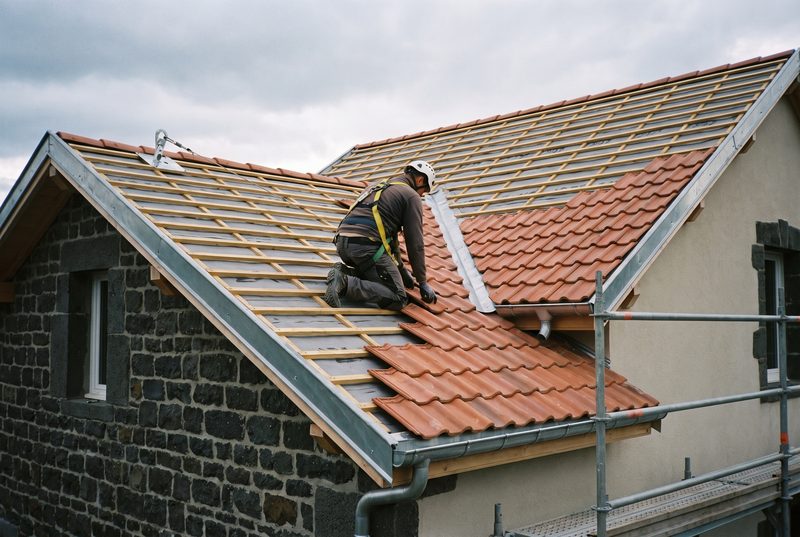 Couvreur posant des tuiles romanes sur une toiture en cours de réfection